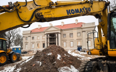 Zdjęcie przedstawiające plac budowy w Nawrze; na pierwszym planie znajduje się wysięgnik koparki i usypana ziemia, w głębi widać remontowany klasycystyczny pałac w Nawrze